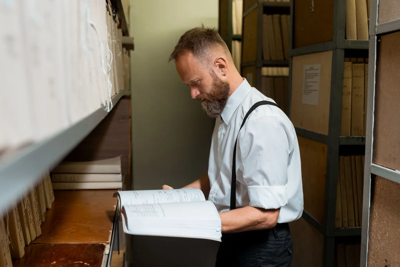 An archivist reading a large bound volume in the stacks