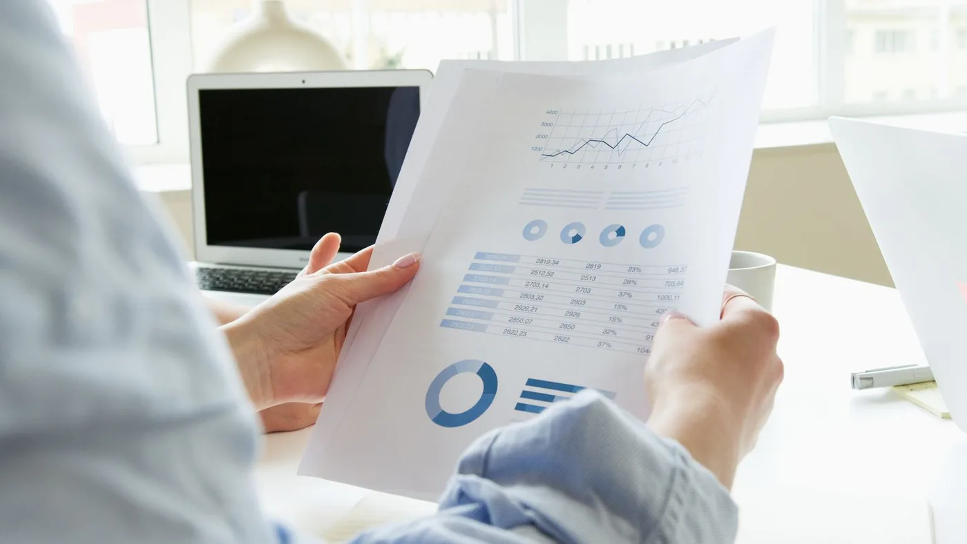 An analyst holding a printed chart beside a laptop