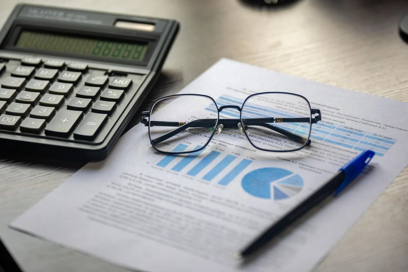 Calculator and glasses over a financial report with blue charts